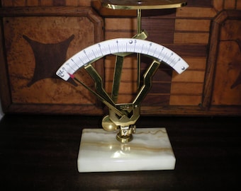 May include: A gold-toned, antique-style scale with a white dial and black markings. The scale is on a white marble base.