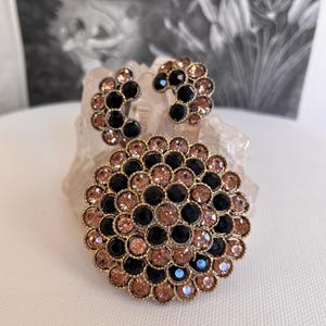 May include: A set of vintage earrings and a brooch featuring a circular design with black and light pink rhinestones.