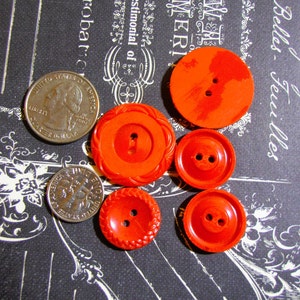 May include: Assortment of six red plastic buttons with two-hole centers. The buttons are various sizes and have different textures.
