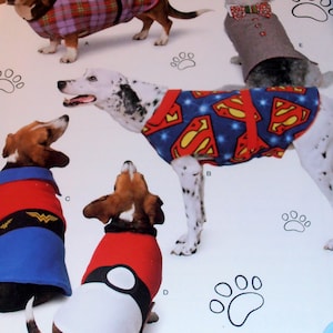 May include: Four dogs wearing different costumes. The first dog is wearing a plaid shirt, the second dog is wearing a Superman costume, the third dog is wearing a Wonder Woman costume, and the fourth dog is wearing a red and white costume with a black circle on the front.