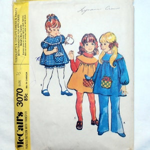 May include: A vintage sewing pattern for children's dresses and pants. The pattern is for sizes 3/2 and includes a transfer for appliques. The pattern is from McCall's and is printed on a yellow background with black text. The pattern shows three girls wearing different dresses and pants.