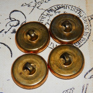 May include: Four antique gold-toned buttons with a raised center and a small hole in the center. The buttons are arranged in a semi-circle on a white surface.