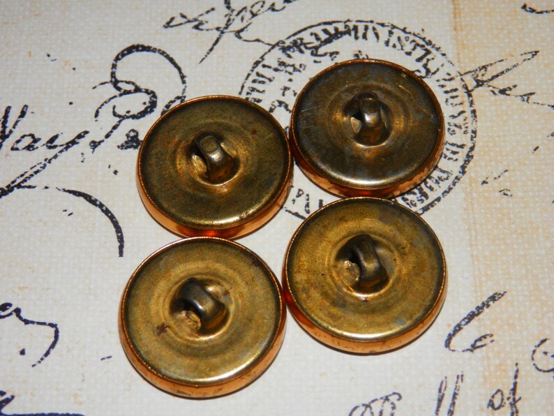 May include: Four antique gold-toned buttons with a raised center and a small hole in the center. The buttons are arranged in a semi-circle on a white surface.