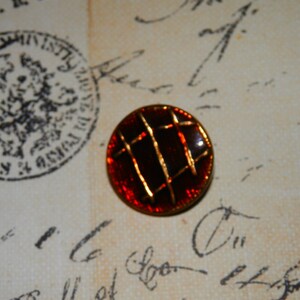 May include: A red and gold button with a geometric design. The button has a shiny, metallic finish.
