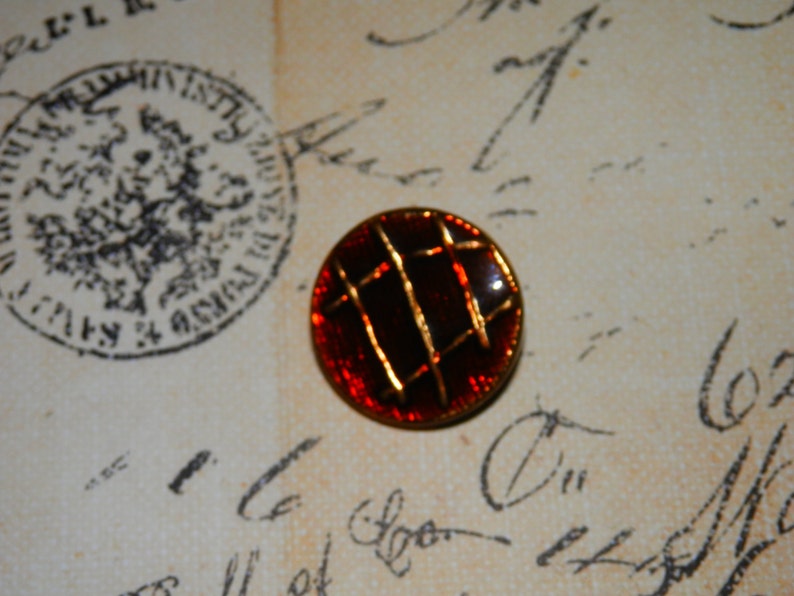 May include: A red and gold button with a geometric design. The button has a shiny, metallic finish.