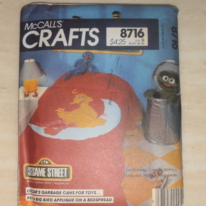 May include: A McCall's Crafts sewing pattern featuring Sesame Street characters. The pattern is for making Big Bird and Oscar the Grouch themed items. The pattern cover shows a red fabric with a yellow Big Bird applique and a white crescent moon. The pattern also includes instructions for making garbage cans for toys. The pattern number is 8716.
