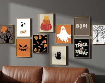 May include: A collection of framed Halloween-themed art prints. The prints feature various designs, including a pumpkin, ghost, spiderweb, and the words "Boo!" and "Trick or Treat." The color palette includes orange, black, and white.