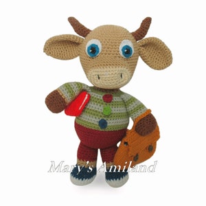 May include: A crocheted brown cow plush toy wearing a green and grey striped shirt with red pants and holding a red heart and a brown and orange object.