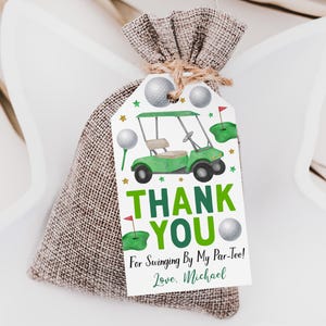 Puede incluir: Una bolsa de arpillera con cordón y una etiqueta de papel rectangular con un carrito de golf verde, pelotas de golf y greens. El texto dice: THANK YOU For Swinging By My Par-Tee! Love, Michael. La etiqueta está atada con un cordel.