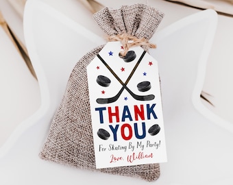 Puede incluir: Una pequeña bolsa de arpillera marrón con cordón y una etiqueta rectangular blanca sujeta con cuerda. La etiqueta muestra dos palos de hockey negros cruzados, discos negros y estrellas rojas y azules. Texto: THANK YOU For Skating By My Party! Love, William.