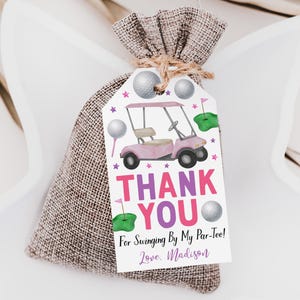 Puede incluir: Una bolsa de arpillera con cordón y una etiqueta de regalo rectangular blanca con un carrito de golf rosa, pelotas, greens de golf y estrellas rosas. El texto dice: THANK YOU For Swinging By My Par-Tee! Love, Madison.