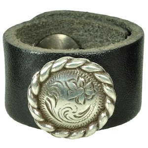 May include: A black leather cuff bracelet with a silver-toned concho featuring a floral design.