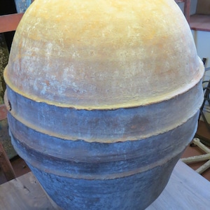 May include: A large, antique-style ceramic lamp with a bulbous, urn-shaped body. The lamp features a two-tone colour scheme, with a light tan upper section and a darker, blue-grey lower section. The lamp sits on a wooden surface.