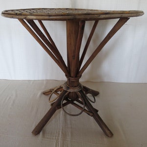 May include: A round, woven, wooden table with a unique, starburst-shaped base. The table has a natural wood finish and is made of woven bamboo.