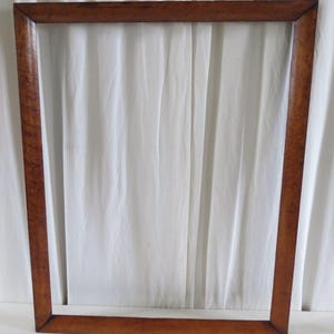Pode incluir: Uma moldura retangular com um acabamento castanho quente. A moldura está vazia, mostrando seu design simples, mas elegante. O grão da madeira é visível, adicionando textura à moldura. As dimensões da moldura não são visíveis.