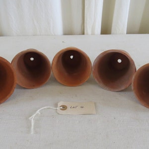 May include: Five terracotta pots arranged in a row, each with a flared rim and a drainage hole at the base. The pots are a warm, earthy brown color. A tag with the text "LOT 4" is attached.