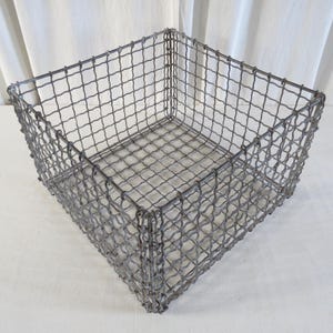 May include: A square, open-top storage basket crafted from grey metal wire. The basket features a grid-like design and a robust, boxy form. The wire is closely woven, resulting in a durable container suitable for diverse storage requirements.