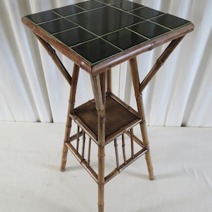 May include: A small, square, bamboo table with a tiled top. The tiles are dark green with a lighter green border. The table has a lower shelf and is made of natural bamboo.