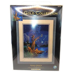 May include: A Dimensions The Gold Collection counted cross stitch kit titled Hidden Spirits. The packaging features a finished design of a person standing by a campfire with a mountain lion, measuring 11 inches by 15 inches, item number 35055.