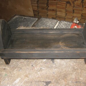 May include: A small wooden bed frame painted black with rounded edges and legs. The bed frame is made of wood and has a simple design.