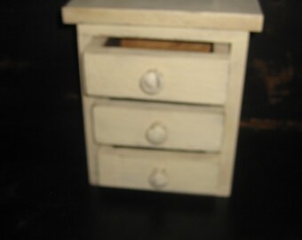 Op de afbeelding: Een klein wit dressoir met drie lades en witte knoppen. Het dressoir is gemaakt van hout en heeft een eenvoudig ontwerp.