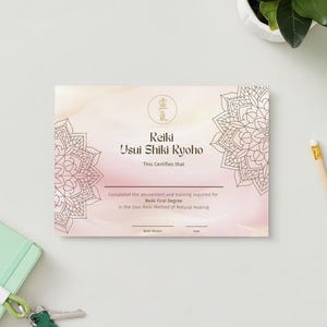 Peut inclure: Un certificat Reiki avec le texte "Reiki Usui Shiki Ryoho" et des motifs floraux de mandala. Le certificat est sur une surface blanche avec un carnet vert, des clés, un crayon et une plante.