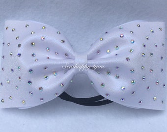 May include: A white satin hair bow adorned with iridescent rhinestones. The bow is tied in a classic shape and attached to a black elastic band. The text "Sewhappy4you" is printed on the bow.