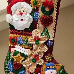 May include: A handmade Christmas stocking with a red background and various felt appliqués. Santa Claus, gingerbread men, a snowman, and other festive shapes are sewn onto the stocking. The top is white with green sequins.