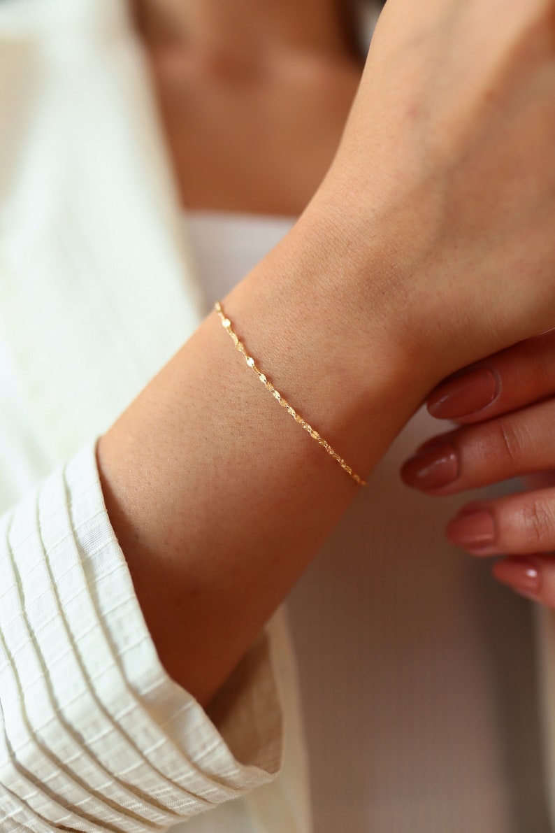 May include: A delicate gold chain bracelet with a twisted design. The bracelet is worn on a person's wrist.