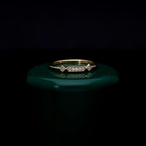May include: A delicate gold ring with a row of small diamonds and two larger diamonds on either side. The ring is on a green surface.