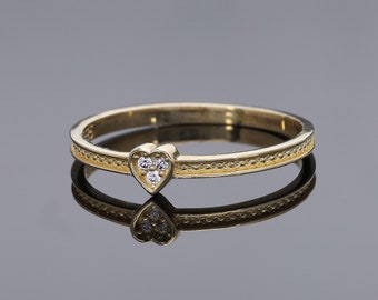 Könnte beinhalten: Ein goldener Ring mit einem herzförmigen Design, das mit drei kleinen Diamanten besetzt ist. Die Ringschiene hat ein strukturiertes Muster.