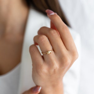 May include: A gold ring featuring a small elephant design. The ring is worn on a person's finger.