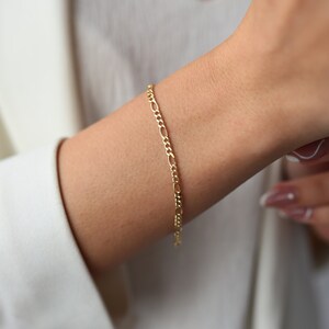Könnte beinhalten: Ein goldenes Kettenarmband mit klassischem Figaro-Gliederdesign.