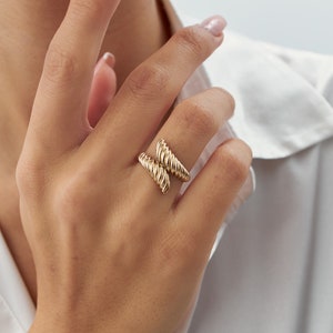May include: A gold-toned ring with a twisted design. The ring is worn on the index finger of a hand.