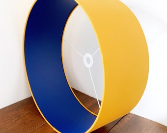 May include: A yellow and blue lampshade with a white inner lining. The lampshade is cylindrical and has a smooth surface.
