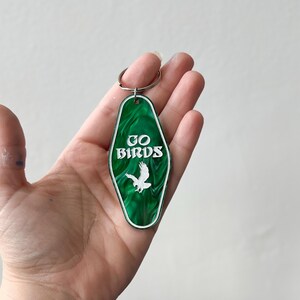 Op de afbeelding: Groene motel sleutelhanger met een witte adelaar en de tekst "GO BIRDS" in wit.