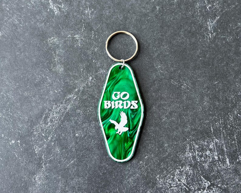 Op de afbeelding: Groene motel sleutelhanger met een wit silhouet van een vogel en de tekst "GO BIRDS".