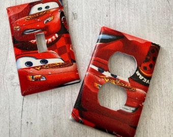 May include: Two red light switch and outlet covers featuring a Cars movie design with Lightning McQueen. The covers are made of a durable plastic material and are easy to install.