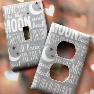 May include: Two light switch covers with a gray background and white text. The text on the covers reads "Love you to the moon and back". The covers feature a crescent moon and stars.