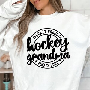 May include: White sweatshirt with a black circle graphic that says "Crazy Proud Hockey Grandma Always Loud" with stars around the circle.