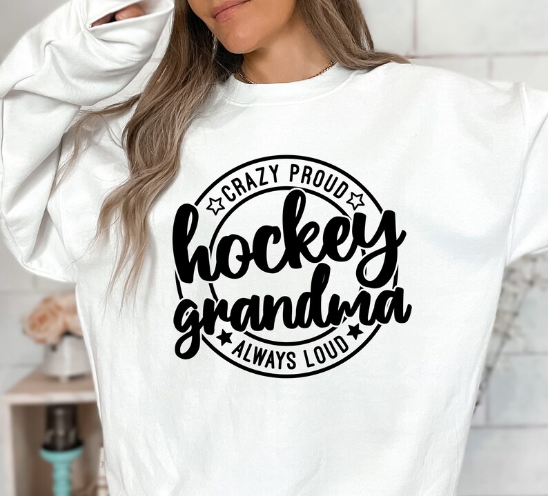 May include: White sweatshirt with a black circle graphic that says "Crazy Proud Hockey Grandma Always Loud" with stars around the circle.