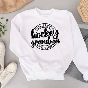May include: White sweatshirt with a black circle graphic that says "Crazy Proud Hockey Grandma Always Loud" with stars around the circle.