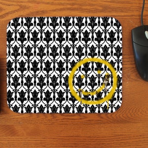 May include: A black and white patterned mouse pad with a yellow smiley face spray painted on it.