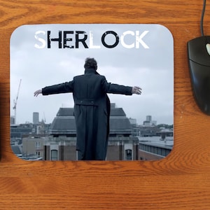 May include: A mouse pad featuring a black and white image of a man standing on a rooftop with the word "SHERLOCK" in white text at the top.