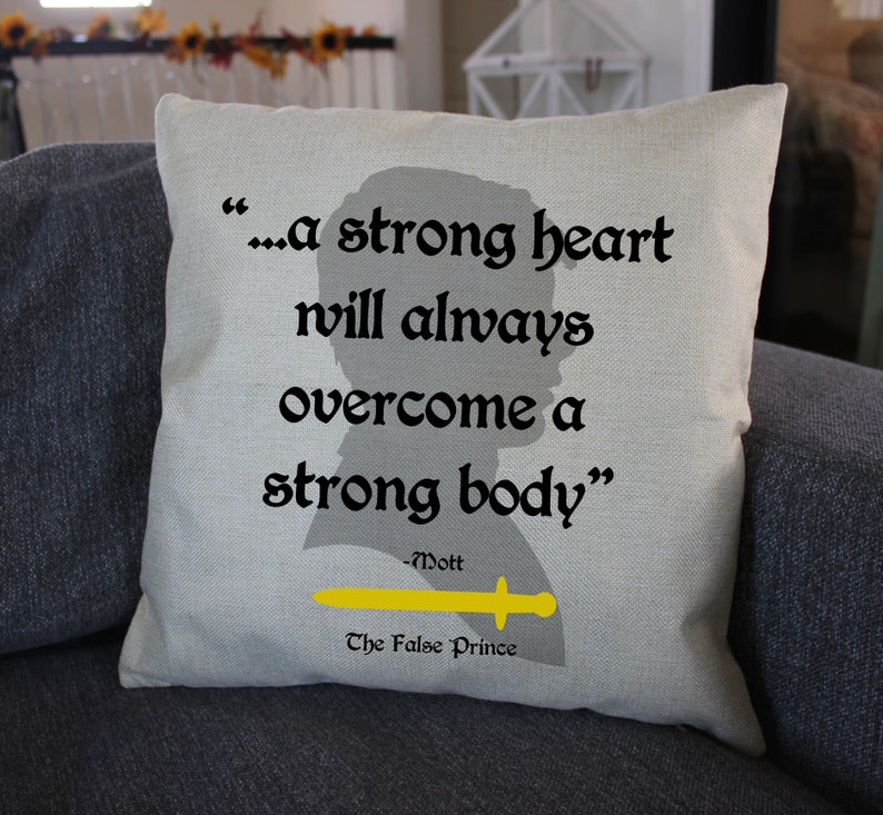 May include: A square, beige throw pillow with the quote "...a strong heart will always overcome a strong body" in black text. A yellow sword graphic is below the quote, with the text "The False Prince".