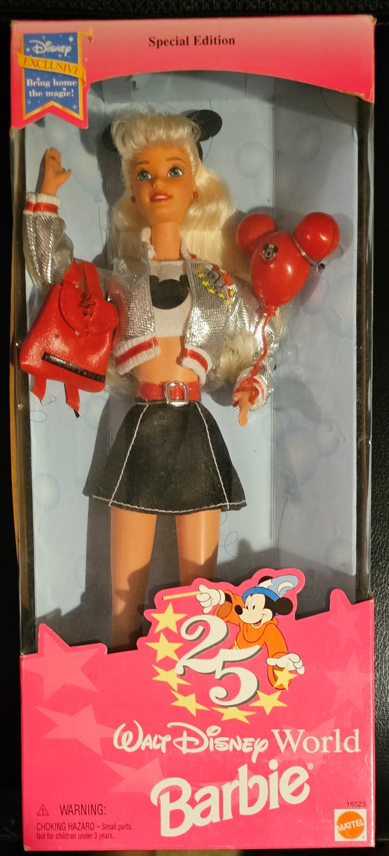 K&ouml;nnte beinhalten: Eine Barbie-Puppe tr&auml;gt eine silberne Jacke mit roten Verzierungen, einen schwarzen Rock und ein wei&szlig;es Hemd mit einer schwarzen Mickey-Maus-Silhouette. Sie h&auml;lt einen roten Mickey-Maus-Ballon und einen roten Rucksack mit der Nummer 25 darauf. Die Puppe befindet sich in einer rosa Schachtel mit dem Text "Walt Disney World Barbie" und "Special Edition" darauf.