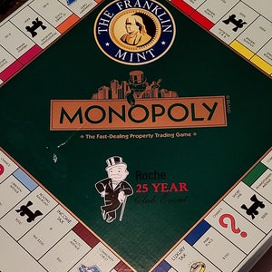 May include: A green Monopoly board game with a 'The Franklin Mint' logo and a Monopoly man figure. The board is titled 'Monopoly' and features the text 'The Fast-Dealing Property Trading Game'. The board also features a Roche 25 Year Club Event logo.