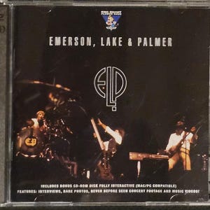 K&ouml;nnte beinhalten: CD-H&uuml;lle f&uuml;r das Album von Emerson, Lake & Palmer. Das Cover ist schwarz mit dem Bandnamen in Wei&szlig; und einem stilisierten Logo. Das Bild zeigt eine Live-Performance der Bandmitglieder. Die H&uuml;lle erw&auml;hnt auch Bonus-CD-ROM-Inhalte.