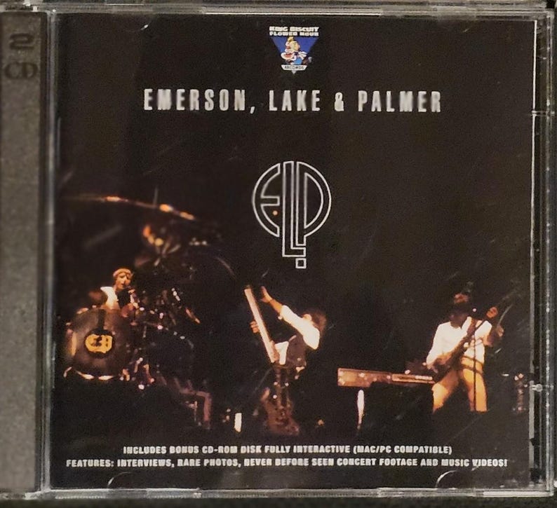 K&ouml;nnte beinhalten: CD-H&uuml;lle f&uuml;r das Album von Emerson, Lake & Palmer. Das Cover ist schwarz mit dem Bandnamen in Wei&szlig; und einem stilisierten Logo. Das Bild zeigt eine Live-Performance der Bandmitglieder. Die H&uuml;lle erw&auml;hnt auch Bonus-CD-ROM-Inhalte.