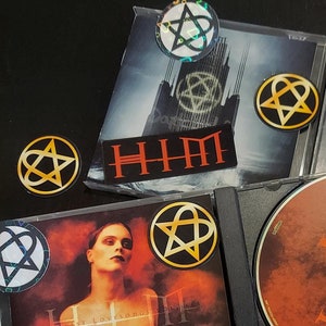 May include: A collection of HIM music CDs and stickers. The CDs feature the band's logo and album art. The stickers are black and red with the band's name and logo.
